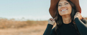 model wearing black shirt and hat smiling in field