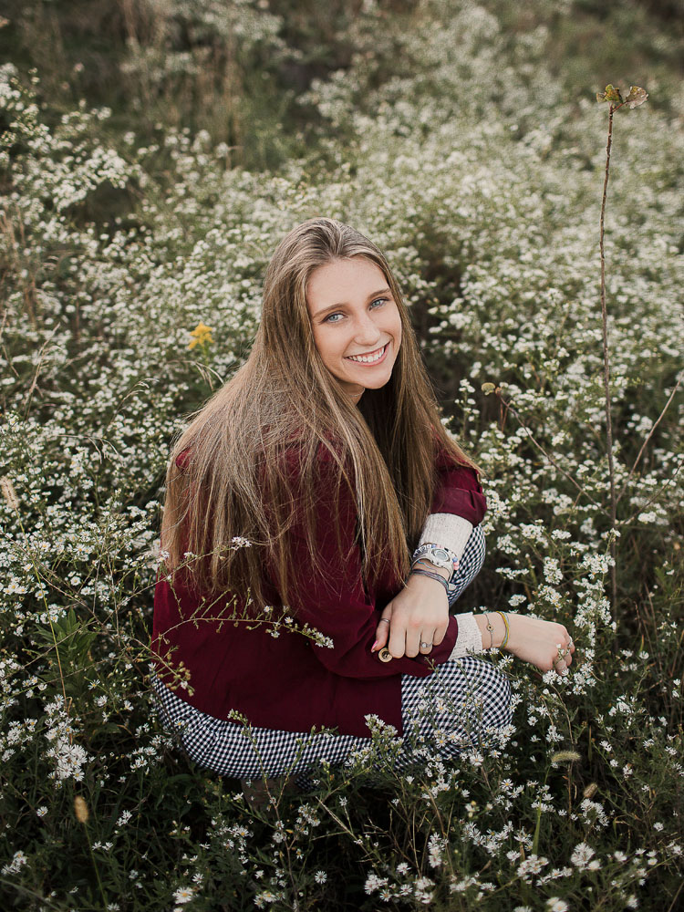 senior girl sitting in beautiful field with flowers