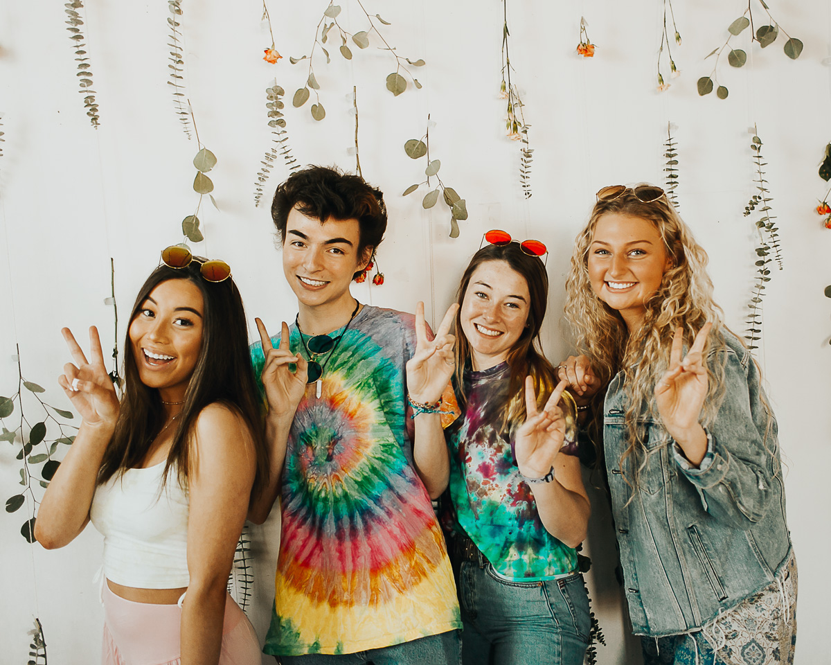 group of young adults wearing tie dye shirts holding up peace sign