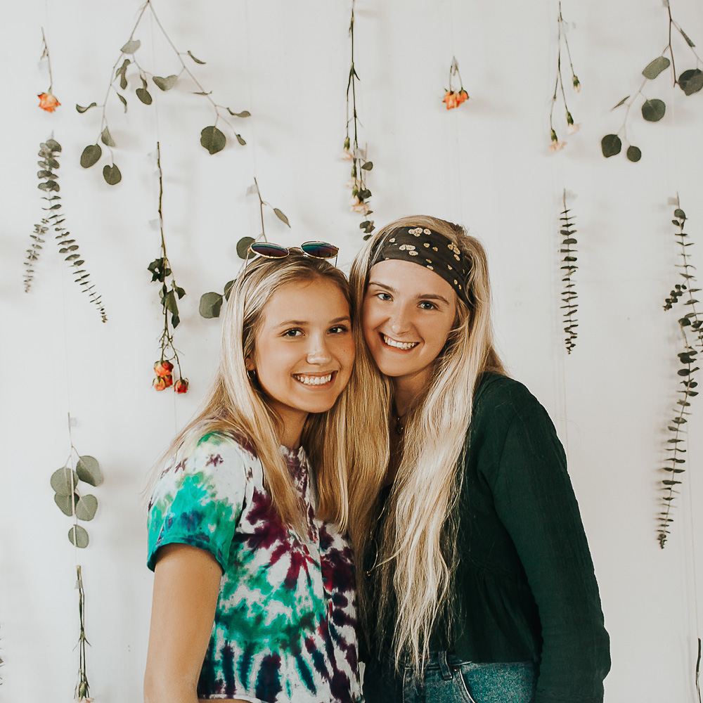 two girls wearing tie dye shirts cheek to cheek on flower background